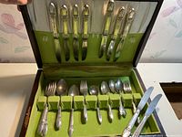 Top view of the open wooden case showing the dinner knives fitted in the upper compartment and other cutlery pieces in the base with green fabric lining.