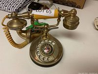 Brass rotary telephone showing the entire phone including handset, rotary dial, and base.