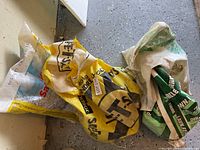 Three bags of driveway salt on garage floor showing varied brands and used condition