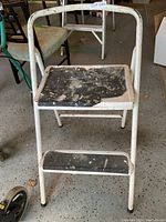 Front view of white metal folding step ladder showing two steps with worn black surfaces and significant paint chipping on top step.
