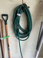 Green garden hose coiled, showing full length and plastic hooks for hanging.