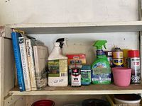 Shelf containing gardening books and various garden and garage chemicals including WD-40 and plant care spray