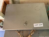 Closed grey metal lock box with key lock and key inserted, slight wear marks visible on surface