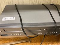 Front and top view of Magnavox combination DVD and VHS player device showing power and operational control buttons with cable across device.