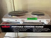 Front view of Salton 2 burner portable electric hot plate on top of its original box showing brand, model and key features.