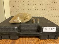 Black hard plastic case with latch and handle, showing two metal sockets placed on top, with a translucent plastic bag covering more sockets.