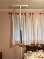 Full vertical view of the white adjustable pole extending ceiling to floor next to a bed and window.