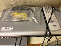 Silver Toshiba DVD Video Player with remote control on top and cables in plastic bag.