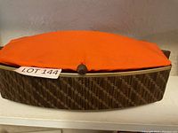 Front view of warming basket with orange fabric cover and wooden knob fasteners.