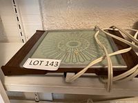 Side angle of warming plate showing wooden frame, frosted glass surface with decorative pattern, power cord wound around it.