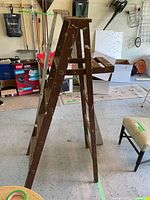 Brown wood step ladder with paint splatters and wear, standing open in a garage