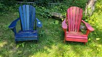 Both Adirondack chairs pictured together outdoors on grass, showing blue and red paint wear.