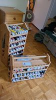 Two wooden paint carry cases filled with numerous tubes of paint and some drawing pens, one vertical with drawer, one horizontal on floor.