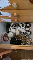 Open drawer showing assortment of watches, bracelets, black beaded evening purse and antique brush, with notable presence of gold-tone chains and several watch bands.