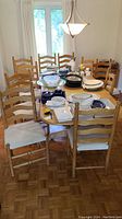 Wide view of 10 wooden dining chairs arranged around a dining table covered in dishes.