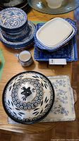 Photo showing various ceramic bowls and dishes including stacked small bowls with blue designs, rectangular baking dishes with a blue checkered edge, a large lidded casserole dish, and a ceramic tray with blue floral pattern.
