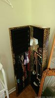 Open view of the wall mounted jewelry armoire showing leopard print exterior and black velvet interior with hanging jewelry.