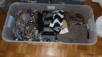 Full overview of folded ladies clothing in a clear plastic storage tote showing multiple colors and patterns.