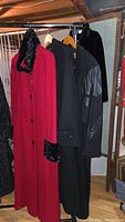 Three ladies medium-sized coats hanging on rack: red coat with faux fur trim, black coat with leather details, plain black coat