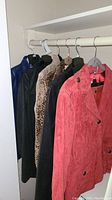 Five jackets hanging on a rack including blue leather, black leather, leopard print, black snakeskin patterned, and red suede jackets