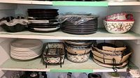 Shelves containing stacked plates, baking dishes, and serving bowls of varied patterns and colors.