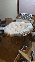 Front view of papasan chair with large beige cushion. Chair frame is wood or rattan and round-shaped with distinct woven backrest lines.