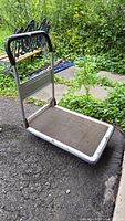 Side angled view of the folding platform cart showing the handle, metal frame, and textured platform surface, capturing the wear and rust spots.