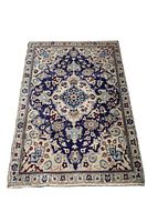 Full view of Persian Naeen rug showing central dark navy and blue medallion with white and light blue floral surrounding, overall light border with smaller flower motifs and fringed edges.