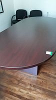 Photo showing the dark wood finish oval top of the boardroom table with part of the table edge visible and chairs around.