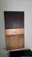 Front view of abstract canvas wall art showing three distinct horizontal textured sections in dark, copper, and bronze colors, mounted on wall.