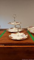 Two Royal Albert cake plates in Country Roses pattern: one two-tier cake plate and one single cake plate with metal handles.