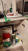 Wide photo showing full countertop with sink, dish drainer, cleaning bottles, and folded tea towels under the sink.