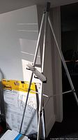 Photo showing the full view of the Quartet easel stand in white metal, with tripod legs and horizontal support for charts. In background is the wrapped flip chart pad.