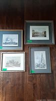 Four framed pictures laid out on a dark wood floor showing architectural and naval scenes.