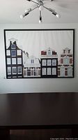 Full view of the framed canvas print depicting Amsterdam buildings on a wall above a table.