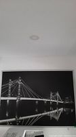 Full image of metal framed black and white wall art showing entire bridge and reflection in water.