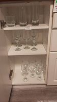 Cupboard shelves with two short tumblers on top shelf, four tall glasses on same shelf, six smaller stemmed glasses on middle shelf, and four larger stemmed glasses on bottom shelf.