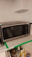 Front view of Danby microwave showing stainless steel exterior and glass door with black frame on countertop with green tape around the edge.