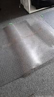 Clear plastic office chair mat with inset cut-out partially rolled showing grip dots and transparency on carpet.