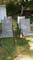 Four stackable patio chairs arranged in a yard. Black metal frames with gray mesh seats and backs noted. Two chairs show mesh fabric pulling on the side.
