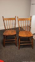 Front view of two vintage wooden chairs side by side, showing spindle backs and solid wood seats.