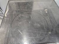 Top view of the turntable under scratched clear plastic dust cover showing the platter and cables.