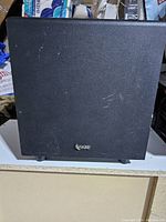 Front view of black Infinity subwoofer with minor scratches on fabric cover and Infinity logo at bottom center.