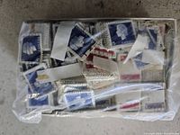 Box with assorted old Canadian postage stamps visible under a clear plastic cover, primarily blue and red stamps with profile portraits.