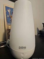 Front view of the white Pore Enrichment personal humidifier showing the conical shape, brand logo, and two control buttons.