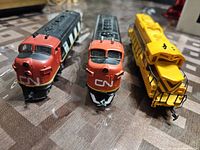 Front view of three vintage train engines: two red and black Canadian National locomotives and one yellow locomotive engine.