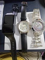 Front view of three untested watches laid flat on white surface showing digital, leather strapped analog, and clear plastic analog watches.