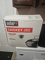 Box showing Weber Smokey Joe Silver 14.5 inch portable charcoal grill branding and image.