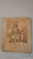 Wood carving of an American Indigenous figure on horseback, detailed on a wooden panel, carved relief work.