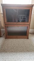 Front view of wooden book shelf with two glass doors and brass knobs on a carpeted floor.